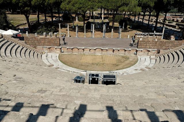 The Roman theatre at Ostia Antica seen from the stage, brick tiers rising towards the umbrella pines
